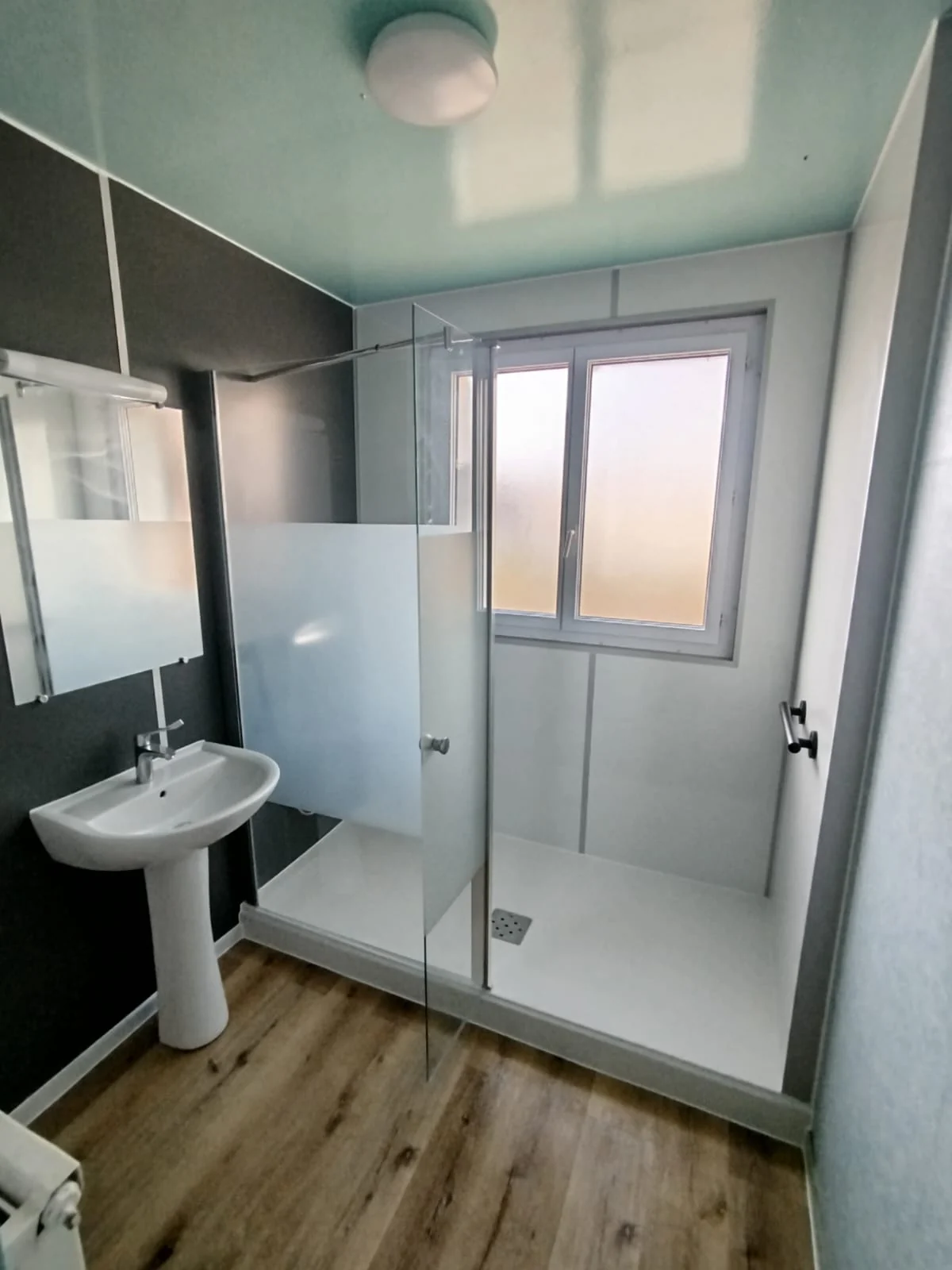 Douche terminée avec panneaux gris, paroi vitrée et fenêtre conservée
